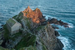Aerial view of Polperro harbour entrance from a birds eye perspective  revealing the restored net loft on top of granite cliff during a golden sunset,  Cornwall, UK.